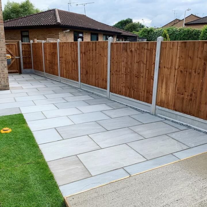 New grey paving slabs along a wooden fence with a small artificial lawn